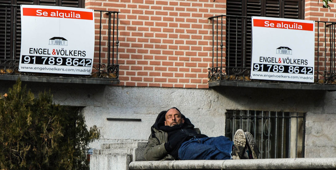 Homeless man next to a rent sign